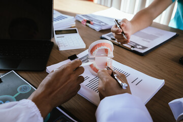 Dental professionals discussing treatment plans with a tooth model and medical documents during a meeting.