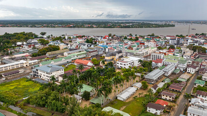 Drone shot of the historic inner city of Paramaribo, featuring colonial Dutch architecture along the Suriname River waterfront under a cloudy sky © Anton Gots