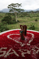A woman stands in a red flower bath overlooking rice terraces and lush tropical hills, creating a...