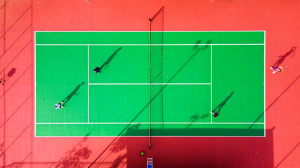 Aerial top down photo of a tennis court with striking colors and contrasting shadows being used by 4 athletes