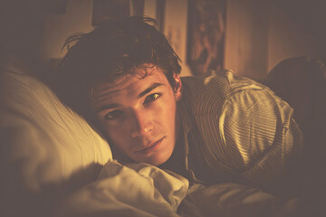 A contemplative young man lies on a bed, gazing intently, illuminated by soft light, creating a warm, introspective atmosphere.