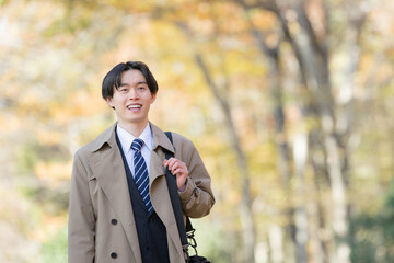 秋の紅葉の屋外でコートを着て営業の外回りなどをする男性