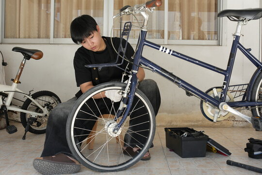 Authentic young tomboy repairing a flat bicycle tire in a garage. Independent female mechanic fixing a bike wheel with tools. DIY maintenance and empowerment concept.