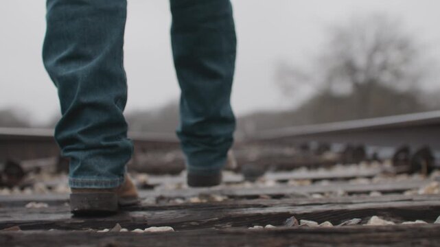 Man Wearing Jeans and Cowboy Boots Walking Along Old Rural Railroad Tracks With Overcast Misty Foggy Weather