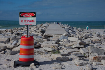 Danger No Trespassing Sign By Rocky Breakwater Pier Over Calm Ocean And Rocky Shoreline at St. Pete Beach, FL. Blue sea, guarded by a bright orange and white construction barrel with a 'Danger No Tres