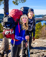 Happy young woman sticks her tongue out at the camera standing beside a young man, both wearing expedition backpacks shot in Killarney Provincial Park on top of mountain room for text