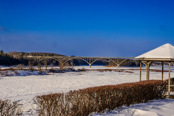 Modern concrete road bridge over snow and ice covered   St. John River  at Hartland New Brunswick with blue sky and room for text