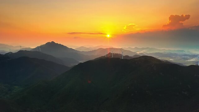 Aerial shot of silhouetted mountain ridges with wind turbines at a golden sunset 