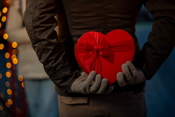 Person secretly holding heart gift box for surprise