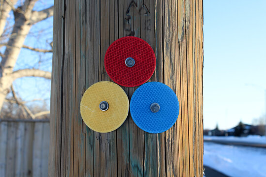 Tres circulos reflejantes de color rojo, azul y amarillo atornillados sobre un poste de madera.