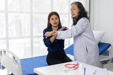 Female doctor examining the arm of a young female patient during a medical consultation in a hospital room, diagnosis and treatment for potential injury or pain.