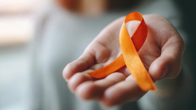 Hand gently offering a vibrant orange ribbon for leukemia awareness and support, spreading hope and compassion through visual storytelling