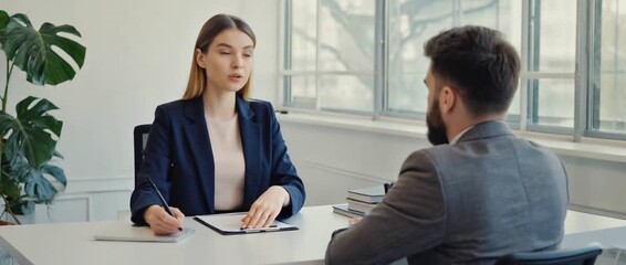 Interview in Office: A focused interaction unfolds as an interviewer and interviewee sit opposite one another in a professional office setting, surrounded by the subtle presence of a potted plant.