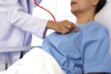 Female doctor examining a senior patient lying in hospital bed using a stethoscope.