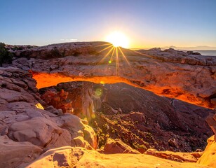 Sunrise illuminates a natural sandstone archway in a desert landscape. Rays beam from the sun as it crests the horizon