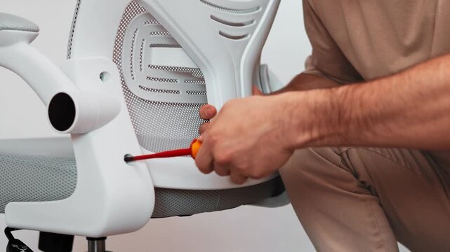 Man carefully uses screwdriver fix bolt modern office chair during home workspace setup. Closeup view highlights precise work, stable design, comfortable assembly process quality ergonomic furniture.
