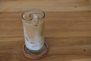 Refreshing iced latte with layered milk and espresso served in a clear glass on a wooden table, perfect for caf&eacute; or lifestyle themes.