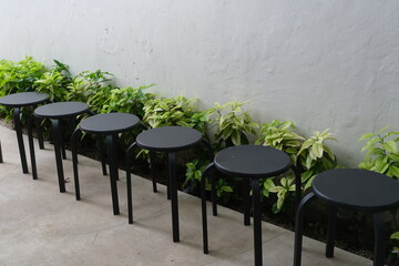 Series of modern black stools lined up beside a planter of green foliage, creating a clean and minimal outdoor seating arrangement.