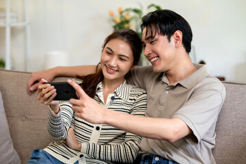 Asian adult couple happy moments mobile phone screen view home living room sofa leisure time content sharing bond connection technology modern lifestyle
