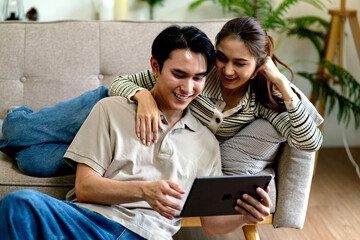 Asian couple adult man woman watching digital tablet happy enjoy online content home living room sofa comfort modern lifestyle technology device use relaxed bonding leisure time together