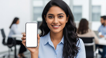 A young Indian businesswoman in a modern office holds up a smartphone with a blank white screen