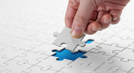 Close-up of a hand fitting the last white jigsaw puzzle piece, with a blue puzzle underneath it. The image symbolizes problem-solving, completion, and strategic connection.