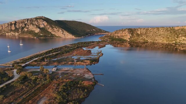 Navarin,Messinia,Gialoval Beach,Aerial view circular pan left from Gialova Lagoon to the Beach.A little channel in between. Lot of sailboats on anchor at the calm bay during sunset.Reflection of cloud