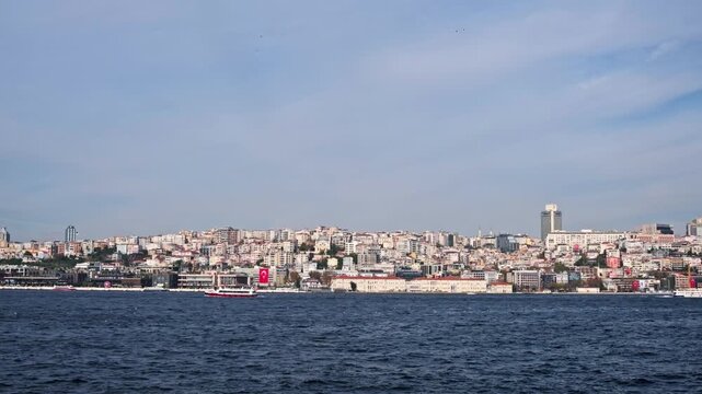A scenic seascape of Istanbul's historic Sarayburnu point. A ferry crosses the water with the ancient walls of Topkapi Palace and lush trees in the background.