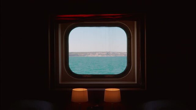 View from inside a cruise ship&rsquo;s lower deck shows gentle ocean waves through a sealed window, creating a quiet, reflective mood ideal for travel and relaxation themes.