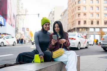 Two women friends browsing smartphone on city street