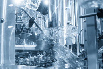 The  empty drinking water bottles  hanging on the overhead conveyor belt for filling process in the light blue scene.