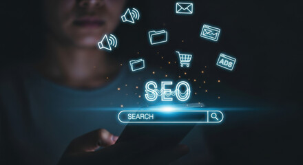 A woman uses her smartphone as glowing SEO icons float above in dark lighting, highlighting digital marketing and search engine optimization concepts.