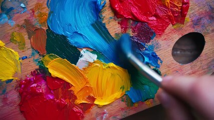 Close up of vibrant oil paints on a wooden palette being mixed with a paintbrush