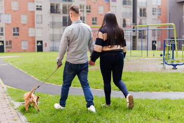 Couple walking dog holding hands in urban park