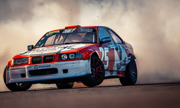 Latvia, Riga 03-05.10.2025. FIA Drifting cup A red and white race car drifting on a track with smoke trailing behind it during sunset