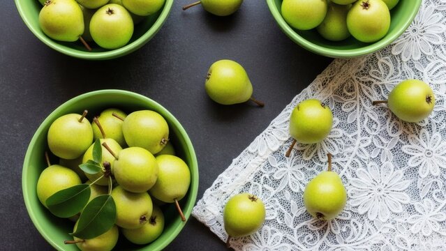 A top-down view of fresh, small green pears in green bowls, with more scattered on a dark surface and a white lace doily, creating a rustic still life composition. - Powered by Adobe