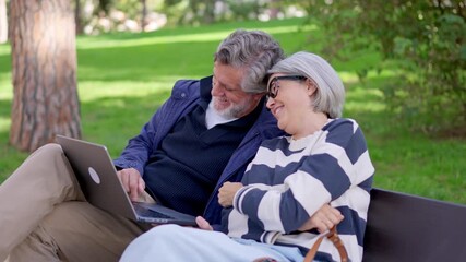 Senior couple using a laptop together in a park - Powered by Adobe