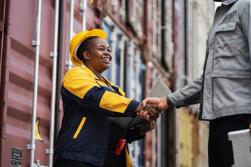 Hand shake African woman logistics workers in high visibility safety gear at shipping container yard	
