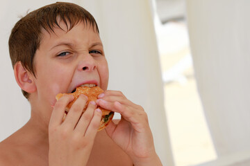 Young boy with wet hair eagerly eating burger