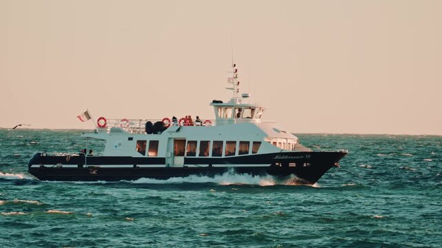 Cannes, France - November 18, 2025: A side view of a passenger ferry named Mediterranee XII, sailing over wavy waters under warm sunset light