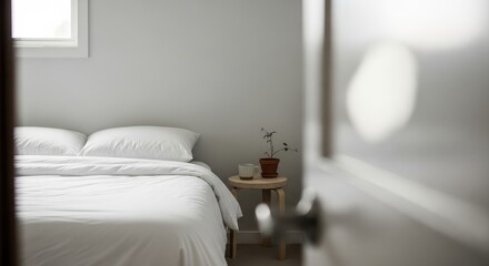 View of a bedroom with white bedding and a plant from behind a doorway