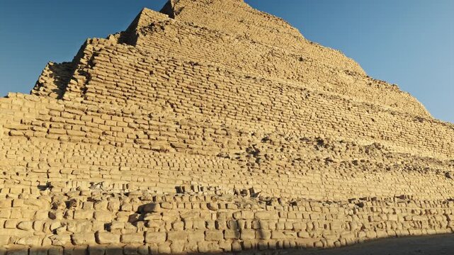 The Step Pyramid of Djoser in the Saqqara necropolis, Egypt, bathed in the warm, golden light of the setting sun.