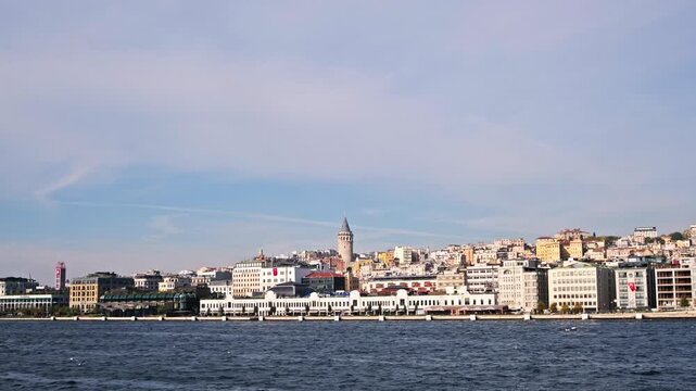 A scenic seascape of Istanbul's historic Sarayburnu point. A ferry crosses the water with the ancient walls of Topkapi Palace and lush trees in the background.