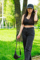 Young woman walking in a sunny park wearing casual black outfit and holding a small bag