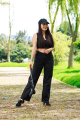 Young woman walking in a sunny park wearing casual black outfit and holding a small bag