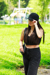 Young woman walking in a sunny park wearing a black cap and casual black outfit
