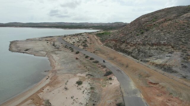 Aerial View of Motorcycle Driving on Coastal Road in Arid Hills