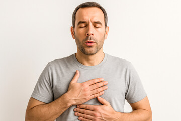 Horizontal studio photo of an adult man holding his chest with eyes closed, showing discomfort/pain on a beige background. Neutral colors, emotional expression make this image suitable for healthcare