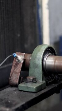 Close-up of an industrial pillow block bearing housing supporting a rapidly rotating metal shaft. A vibration sensor is mounted on the bearing block, indicating machinery monitoring.