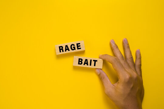 male hand put rage bait words on wooden blocks isolated on yellow background